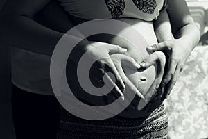 Portrait of a Couples hands making heart shape over her pregnant belly. Black and white photo