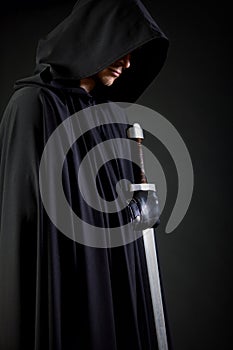 Portrait of a courageous warrior wanderer in a black cloak and sword in hand.