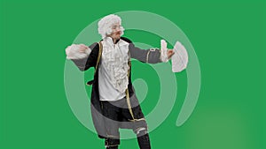 Portrait of courtier gentleman in black historical vintage suit and white wig, dancing merrily with a fan in his hands