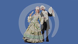 Portrait of courtier lady and gentleman in historical vintage costumes and wig is waving a fan. Young woman and man
