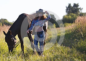 Portrait of a cowgirl - young woman with horse in meadow at summer day