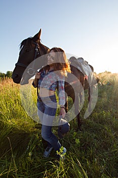 Portrait of a cowgirl - young woman and horse in the meadow at sunny summer