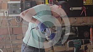 Portrait of craftsman engineer focused on drilling a hole with tool on the background of a small workshop. Concept of