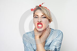 Portrait of crazy angry young woman in casual blue denim shirt with makeup and red headband standing, choke sheself and clenching