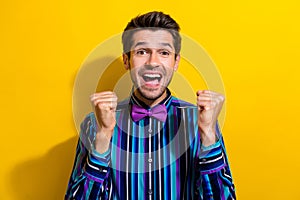 Portrait of crazy eccentric guy dressed stylish shirt bow tie clenching fists win betting isolated on vibrant yellow