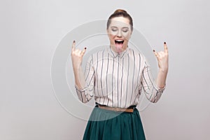 Portrait of crazy funny beautiful young woman in striped shirt and green skirt and collected ban hairstyle, standing with rock