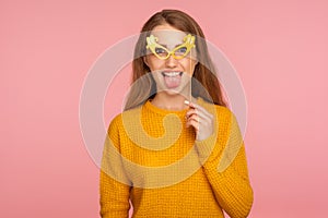 Portrait of crazy funny joyful ginger girl in casual sweater wearing fake paper eyeglasses and sticking out tongue, making faces