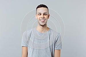Portrait of crazy loony funny young man in casual clothes with beveled eyes showing tongue isolated on grey wall photo