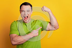 Portrait of crazy masculine brutal guy indicate finger biceps scream on yellow background