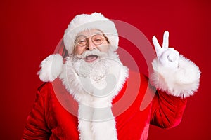 Portrait of crazy stylish santa claus enjoy x-mas christmas make v-sign wear red costume cap white gloves isolated over