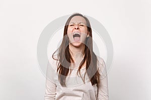 Portrait of crazy weird frustrated young woman in light clothes keeping eyes closed, screaming isolated on white
