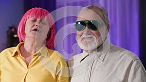 portrait of creative cheerful female and male pensioners in wig and stylish glasses having fun smiling and looking at