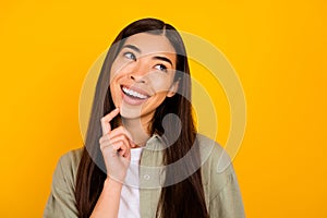 Portrait of creative minded girl toothy smile finger touch chin look empty space isolated on yellow color background