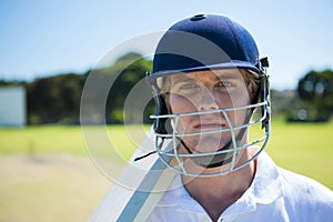 Portrait of cricket player holding bat while wearing helmet at field