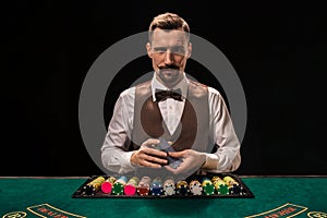 Portrait of a croupier is holding playing cards, gambling chips on table. Black background