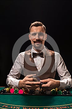 Portrait of a croupier is holding playing cards, gambling chips on table. Black background