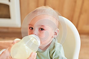 Portrait of a crying baby drinking milk from a baby bottle