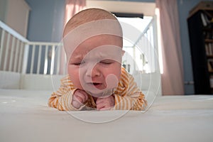 Portrait of crying baby girl lying alone on bed.