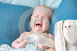 Portrait of a crying baby on a green bed in the bedroom. Child`s emotions