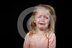 Portrait of a crying blond baby girl on black background