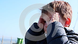 portrait of crying boy kid standing alone outdoors holding heat with two hands