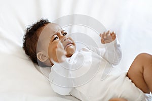 Portrait Of Crying Little Black Baby Wearing Bodysuit Lying On Bed