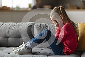 Portrait Of Crying Little Girl Sitting On Couch At Home