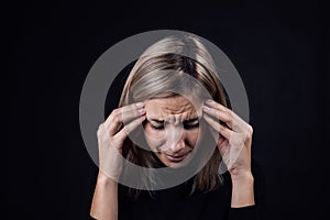 Portrait of crying woman with face down hand fingers touching temples on black background. Victim of physical and