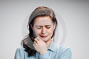 The portrait of a crying young lonely woman on gray