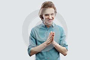 Portrait of cunning handsome long haired blonde young man in blue casual shirt standing and looking at camera with bitchy plan