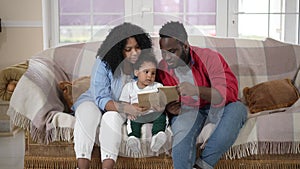 Portrait of curios adorable little boy listening couple of parents reading fairy tale. Happy African American toddler