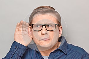 Portrait of curious man placing hand near ear and eavesdropping