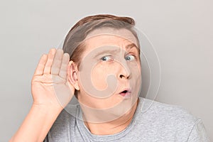 Portrait of curious man placing hand near ear and eavesdropping