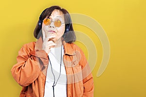 Portrait of a curious and thoughtful middle aged woman with headphones and hipster glasses - yellow background with copy space on