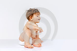 Portrait of curious toddler boy, baby in diaper crawling isolated over white studio background. Playing child
