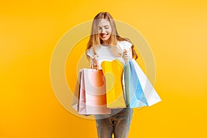 Portrait of a curious young woman , after a good shopping, looking inside the bag, isolated on a yellow background