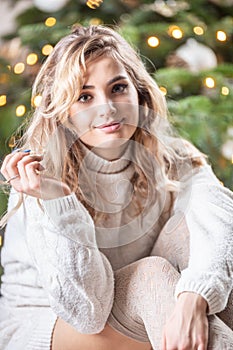 Portrait of a curly blonde woman in white sweather in front of a christmas tree