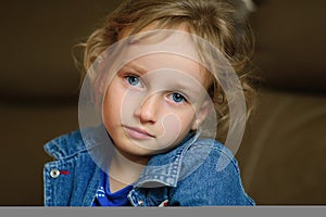 Portrait of a curly blue-eyed girl with a calm look. She is wearing a denim vest