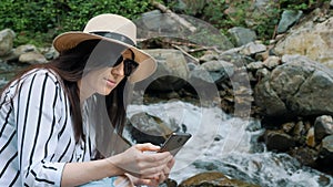 Portrait of curly girl in forest looking in smartphone hiking near river. Young woman hiker in mountain hike finding