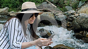 Portrait of curly girl in forest looking in smartphone hiking near river. Young woman hiker in mountain hike finding