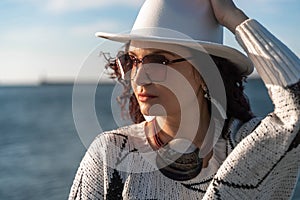 Portrait of a curly haired woman in a white hat and glasses on the background of the sea.