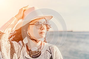 Portrait of a curly haired woman in a white hat and glasses on the background of the sea.