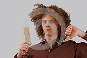 Portrait of a curly-haired young man with a wooden comb in magnificent hair dissatisfied with the result on a gray isolated