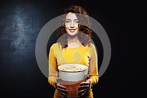 Portrait of curly woman holding popcorn bucket looking straight