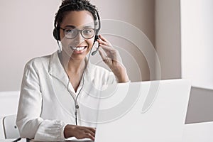 Portrait of customer service assistant talking on phone. Woman wearing headset working on laptop computer.