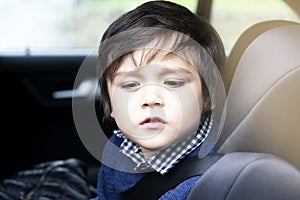 Portrait cut lilttle boy sitting in a car in safety chair, Adorable toddler boy sitting in car seat, Child in car seat looking dow