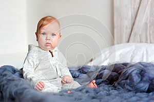 Portrait of cute 8 month old baby girl sitting on the bed on oversize knitted blanket