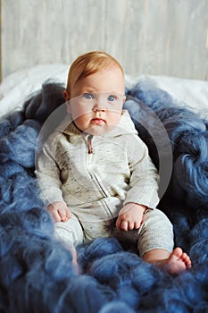 Portrait of cute 8 month old baby girl sitting on the bed on oversize knitted blanket