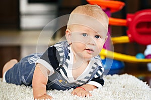 Portrait of cute adorable blond Caucasian smiling baby boy with blue eyes lying on floor in kids children room