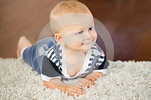 Portrait of cute adorable blond Caucasian smiling baby boy with blue eyes lying on floor in kids children room